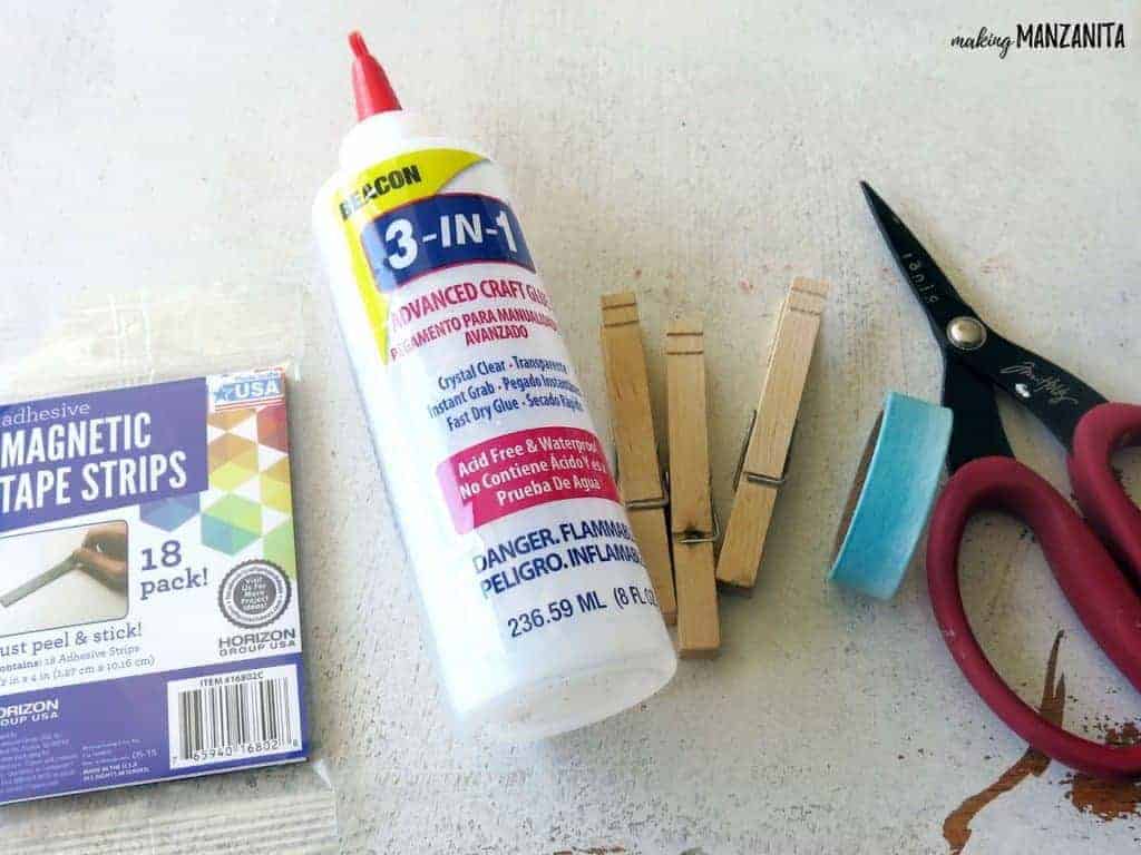 Magnetic strips, craft glue, wood clothespins, washi tape and scissors are laid out on a white table. These are the supplies you need to make quick DIY clothespin magnets.