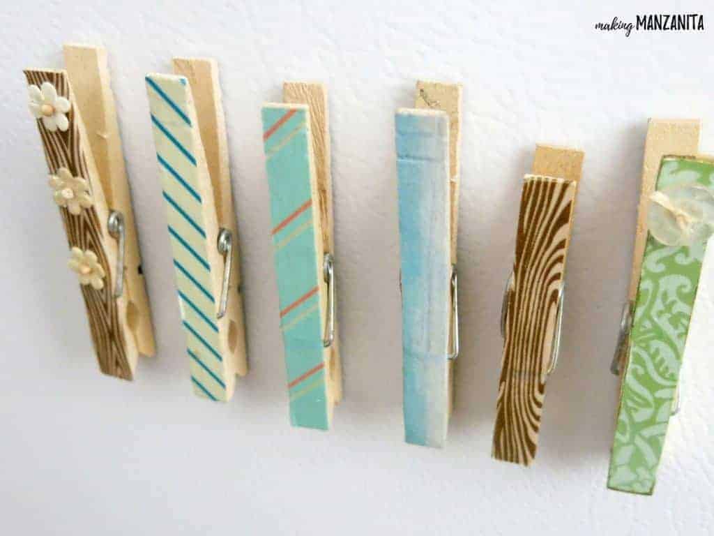 A row of DIY clothespin magnets stuck to a white surface. Each magnet has a different pattern; two feature brown stripes, three are covered with blue patterned washi tape, and the last in the row is a green and white paisley pattern.