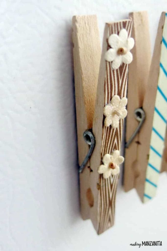 A closeup image of a clothespin magnet decorated with brown striped washi tape and small fabric flowers.