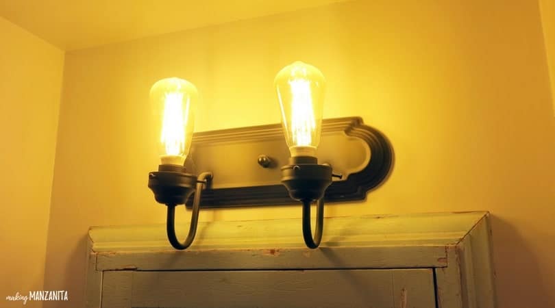 This vintage sconce is mounted over the bathroom mirror; it has two vintage lightbulbs in black metal holders.