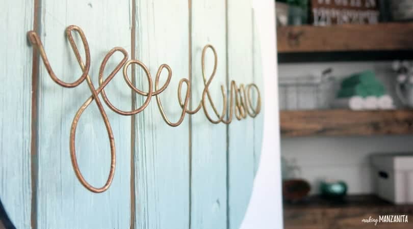 A close up look at a teal wood sign with brass wire twisted to read 