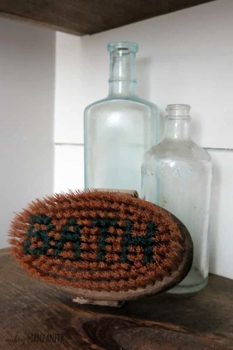 Vintage glass bottles and brush on a wood shelf with shiplap walls in background