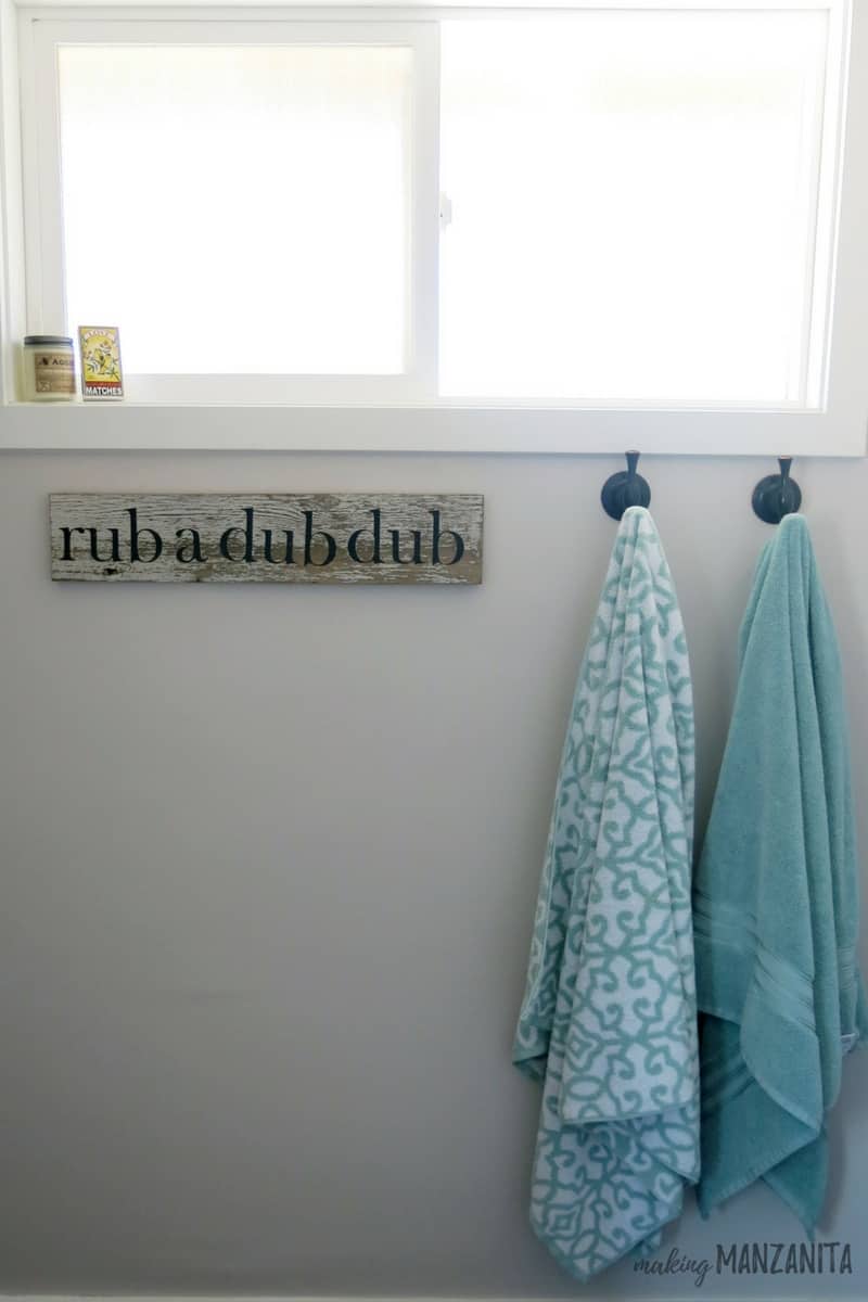 Gray wall painted with Burnished Clay by Behr in bathroom with towels hanging on hooks and rub a dub dub sign under window