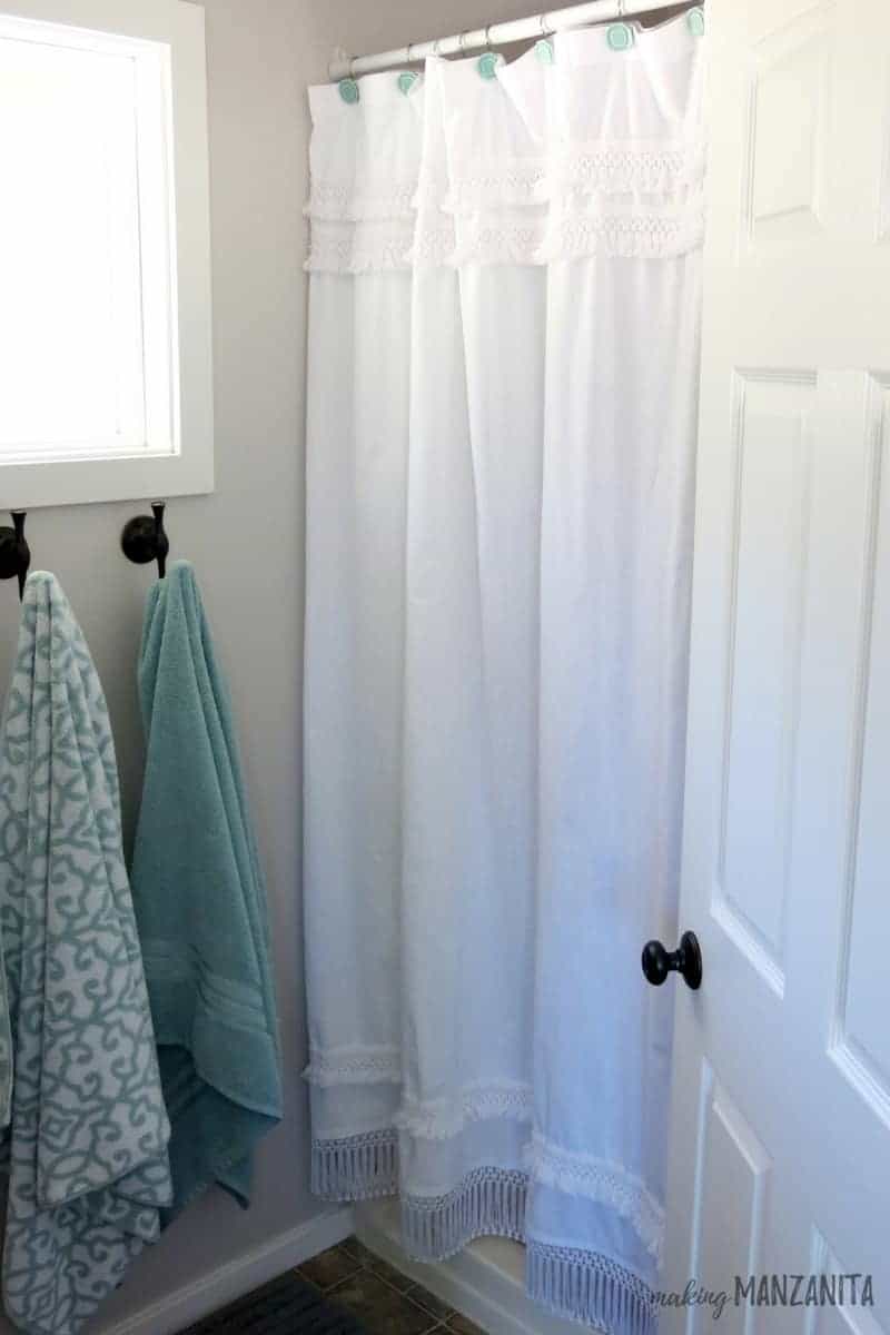 The white macrame shower curtain completes the look in our farmhouse master bathroom; next to the shower curtain, two metal towel hooks are mounted to the wall.