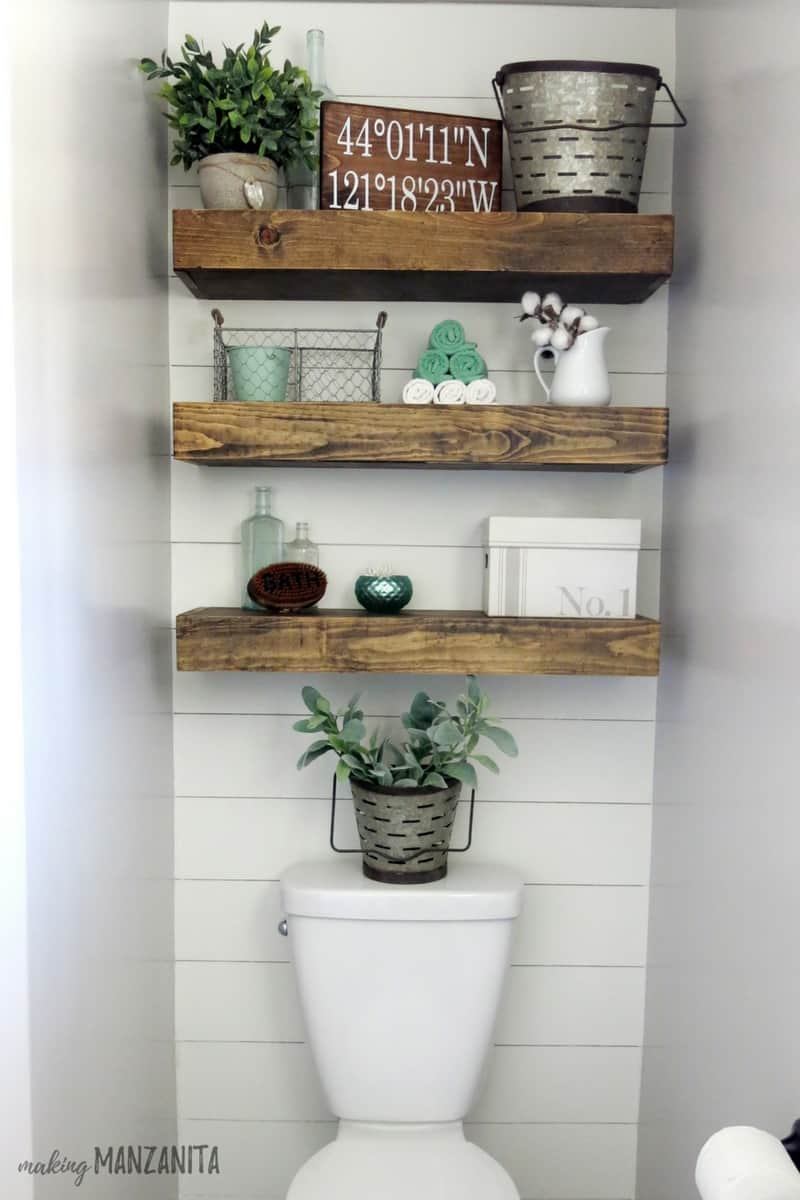 A closer look at the shiplap wall behind the toilet, with mounted floating shelves decorated with farmhouse trinkets.