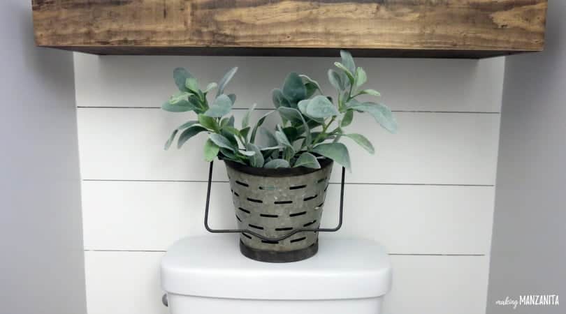 A lambs ear plant sits in a galvanized bucket on the back of the toilet in the farmhouse master bathroom.