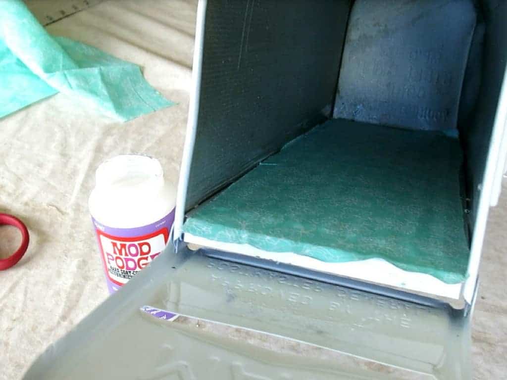 Inside view of the cleaned old mailbox with fabric lined on the inside beside a bottle of mod podge