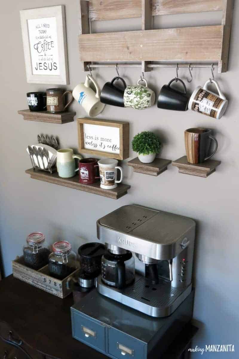 A vintage dresser works great for creating a home coffee station in your living room or kitchen with coffee beans, a coffee grinder, and a coffee maker on top of a metal drawer. On the wall, there's a wood mug hanger floating shelves holding mugs and a farmhouse sign