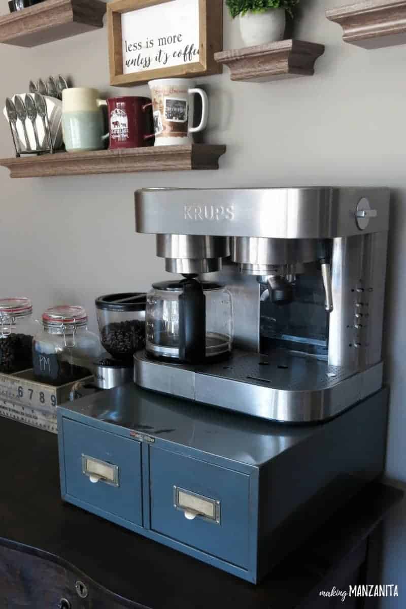 This vintage dresser is perfect for our home coffee station with a metal box holding a KRUPS coffee maker on top with a coffee grinder, coffee beans, and coffee mugs