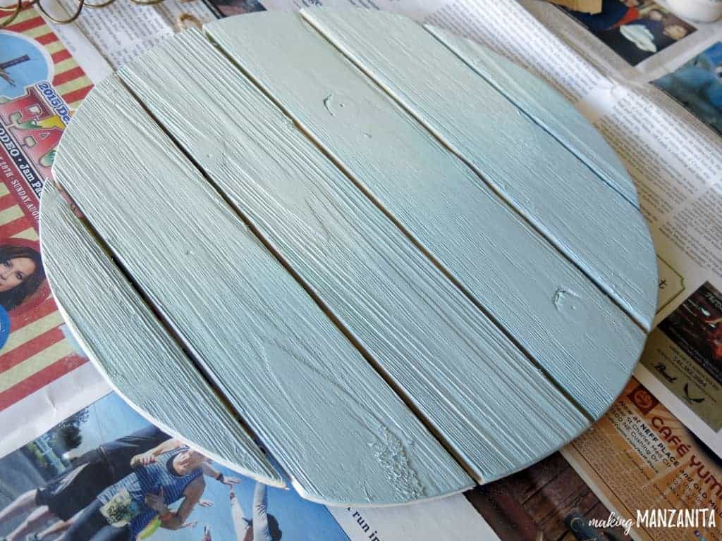 Creating an ombre paint effect on a circular wood sign by painting the lower half of the sign with a slightly darker paint color.