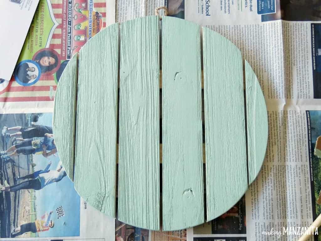 A circular wood sign sits on newspaper, painted a mint green.