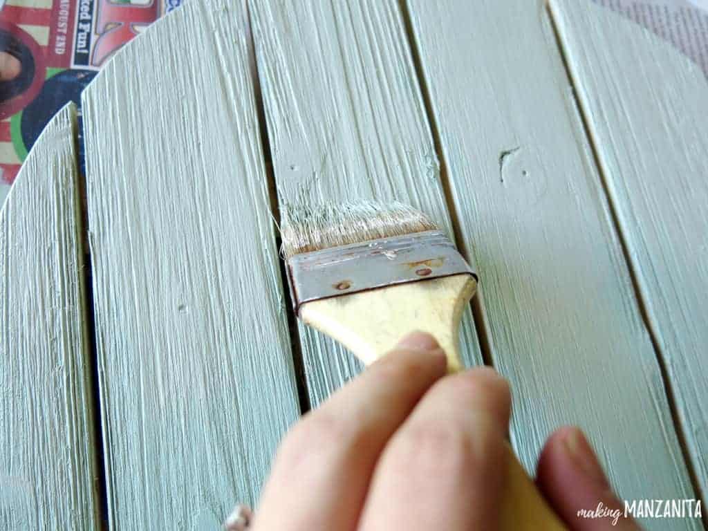 Using a paint brush to paint the ombre wood sign with the base color - a light mint green.