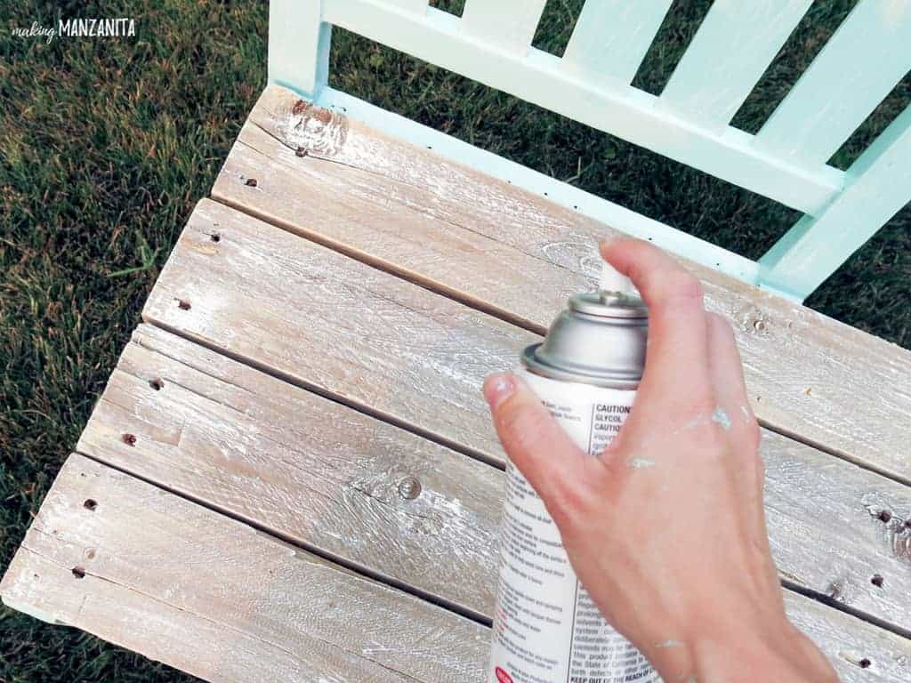 Using a spray acrylic coating to seal the seat of the bench, which is attached to the two painted upcycled chairs.