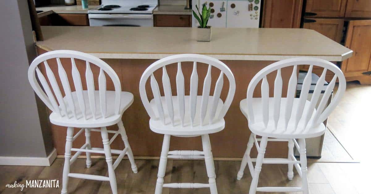 Three bar stools painted with white chalk paint, lined up at a kitchen breakfast bar.
