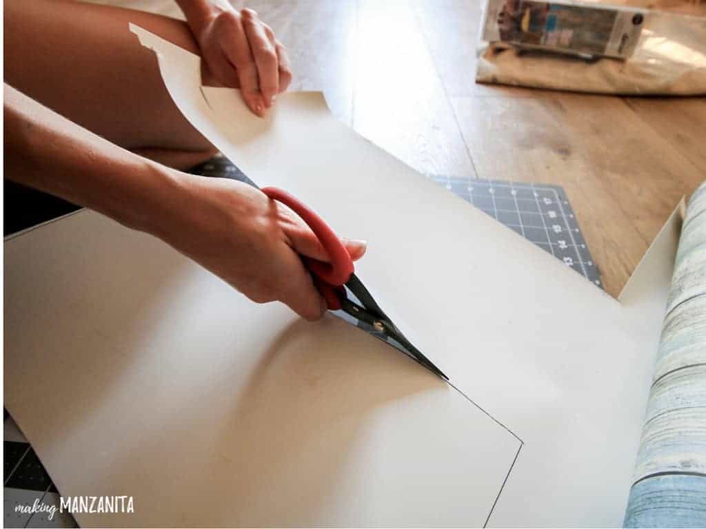 Cutting out peel and stick wallpaper for the sides of dresser drawers with scissors
