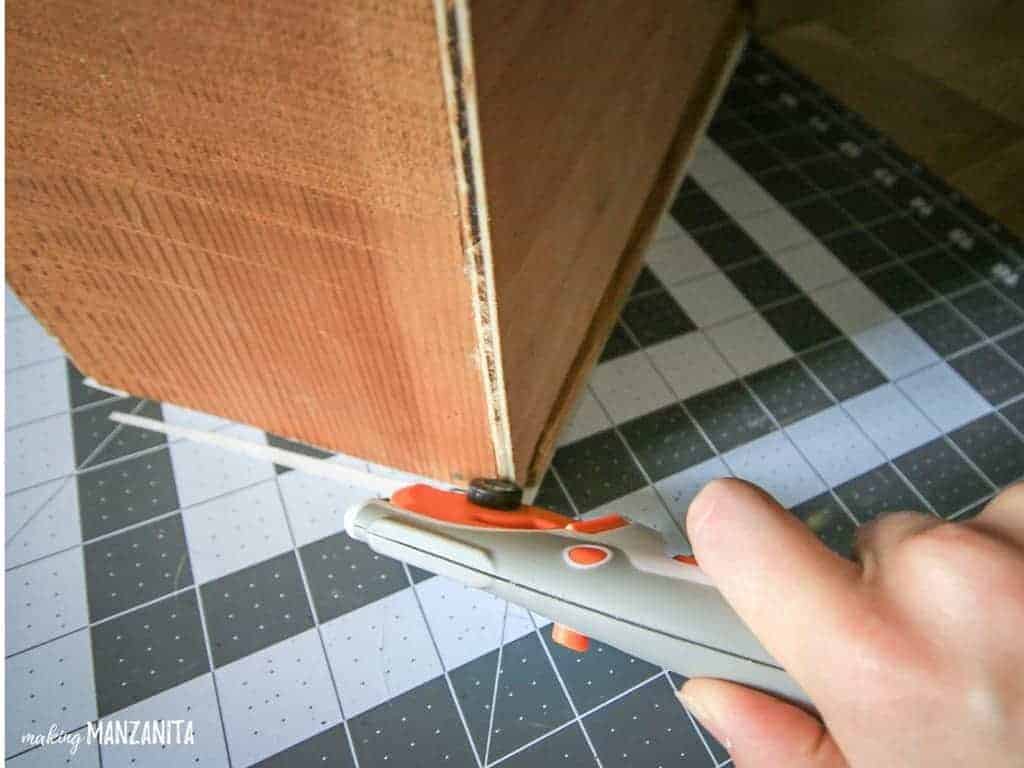 Trimming off the excess wallpaper  from side of dresser drawer with a rotary cutter on a cutting mat