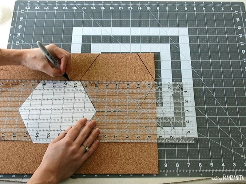 Woman holding a marker and ruler tracing the hexagon shape on the cork board