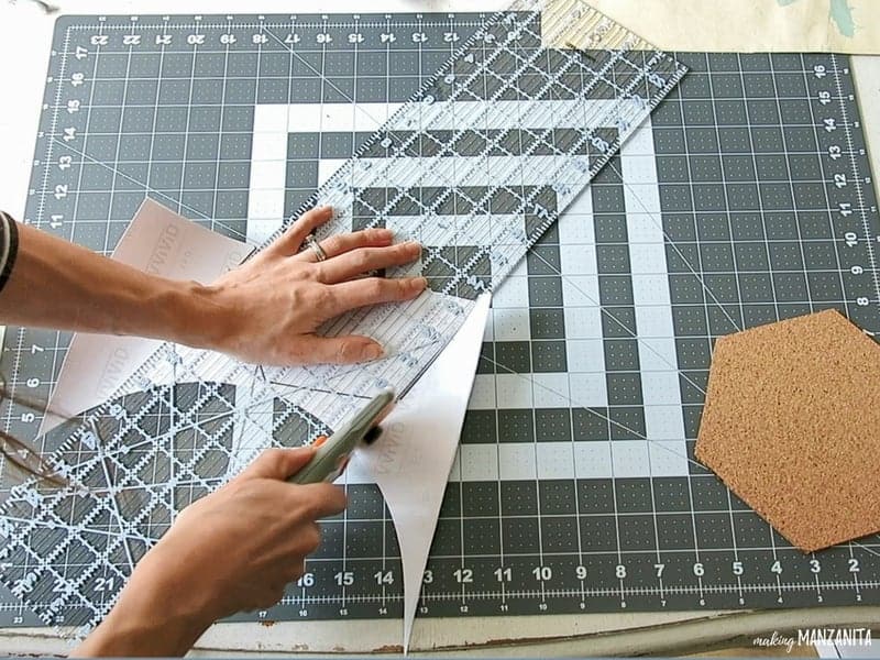 Woman cutting a marble contact paper with rotary cutter and ruler and hexagon cork board beside it