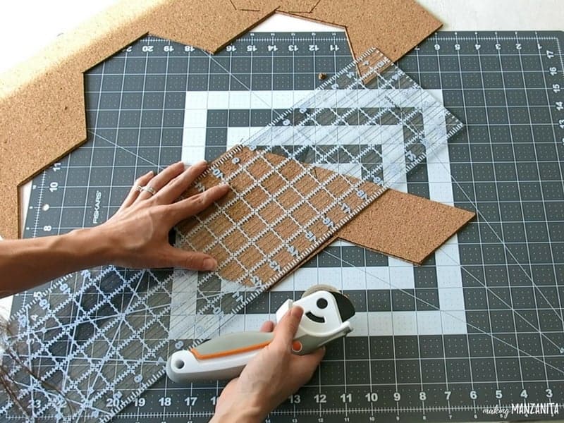 Woman holding a clear acrylic ruler and rotary cutter cutting the cork board into hexagon shapes for DIY hexagon cork boards