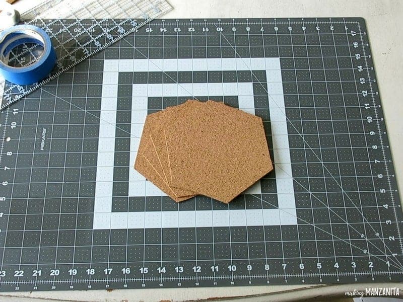 Cork board cut into hexagon shapes on top of the cutting mat with ruler and painter's tape beside it