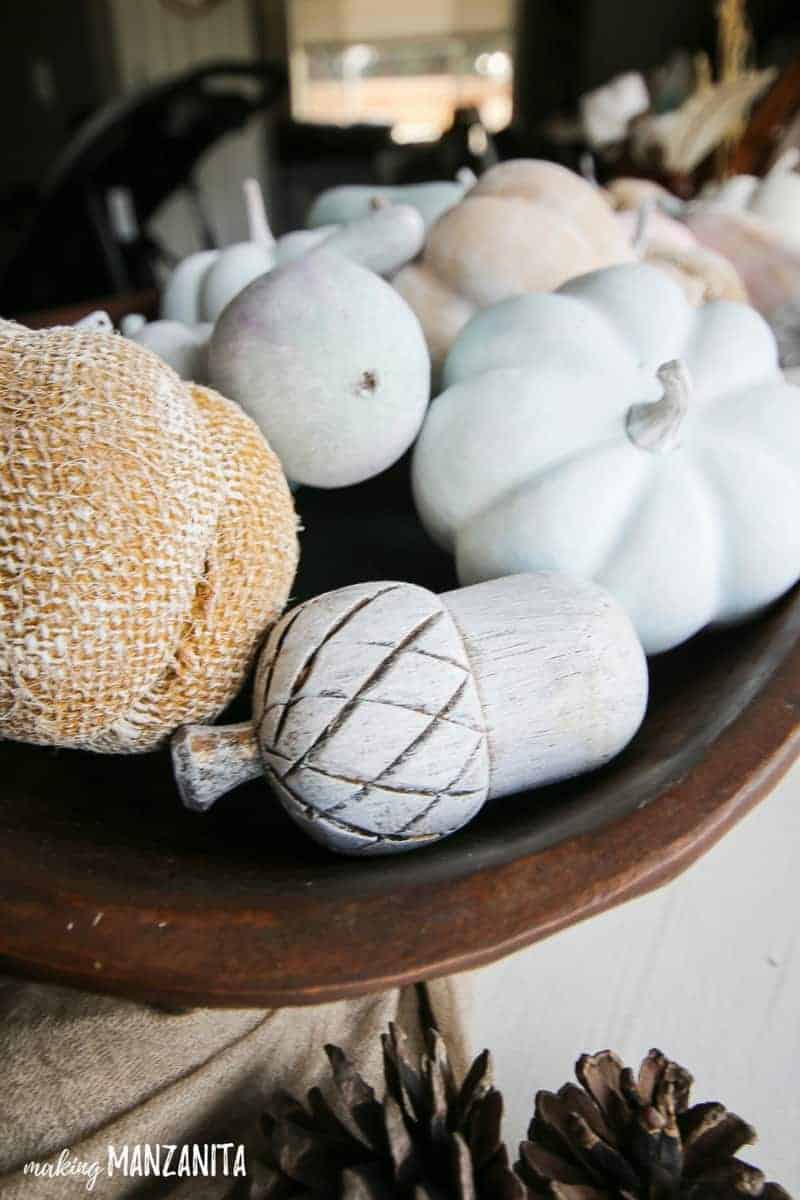 Close up shot of painted pumpkins, goards and acorns in a wooden bowl for table decorations