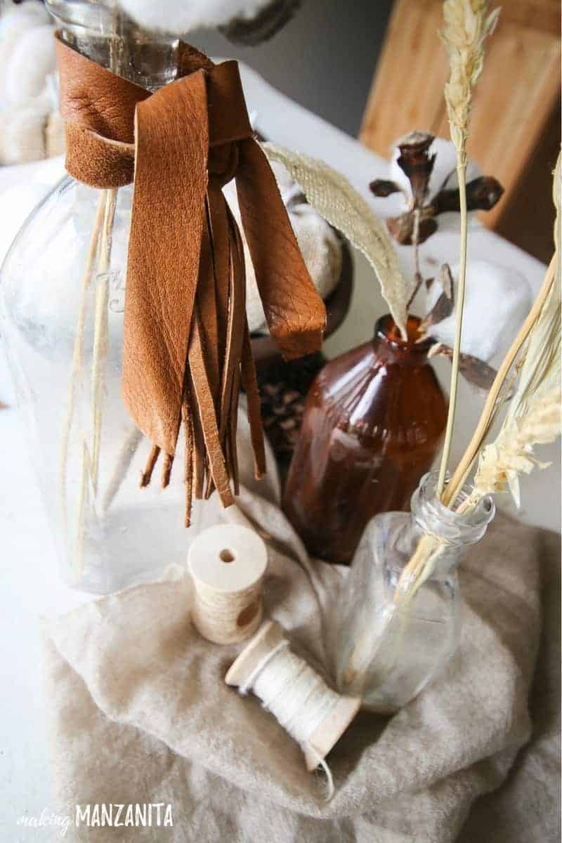 Vintage bottoms with leather wrapped around the tops with wheat in them on top of tan fabric with spools of natural twine to decorate a table for fall with farmhouse style