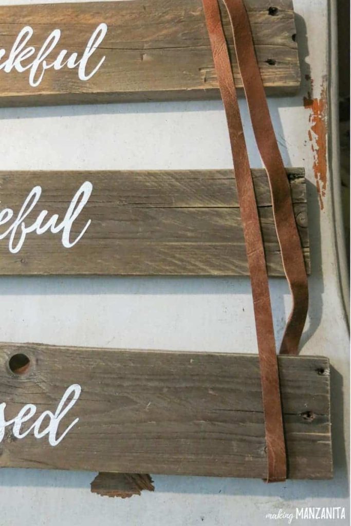 Long leather strips rest over three planks of pallet wood, each painted with the words "thankful", "grateful", and "blessed"