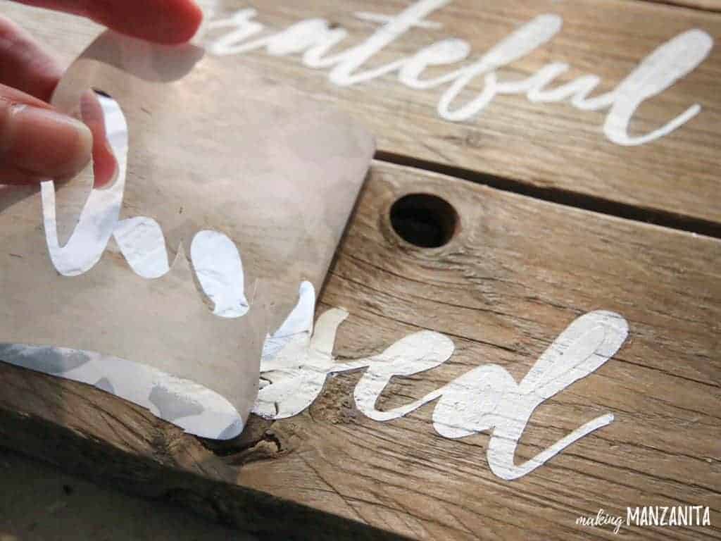 A woman peels the stencil off the wooden board, revealing a perfectly painted stencil of the wood 