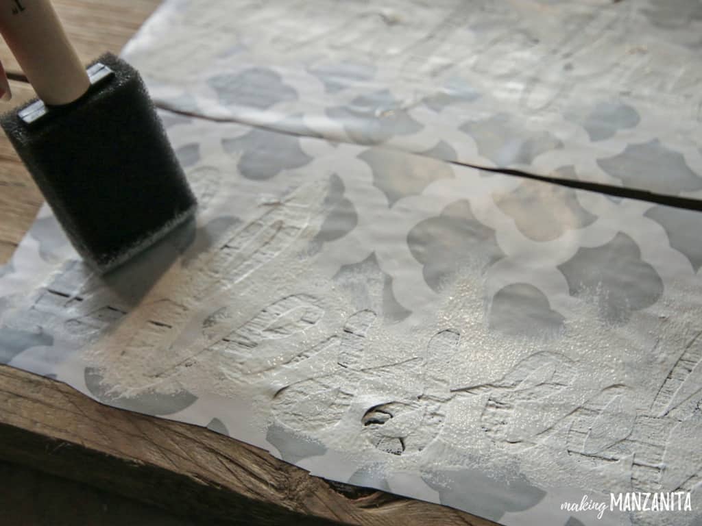 Painting over stencil on the wood  sign using a foam paint brush