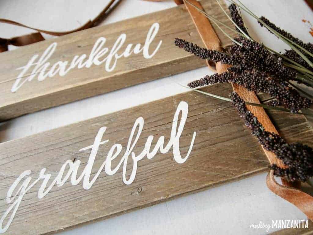 A closeup image of the leather thankful-grateful-blessed wood sign, displayed with dried grass resting to the side of the sign.