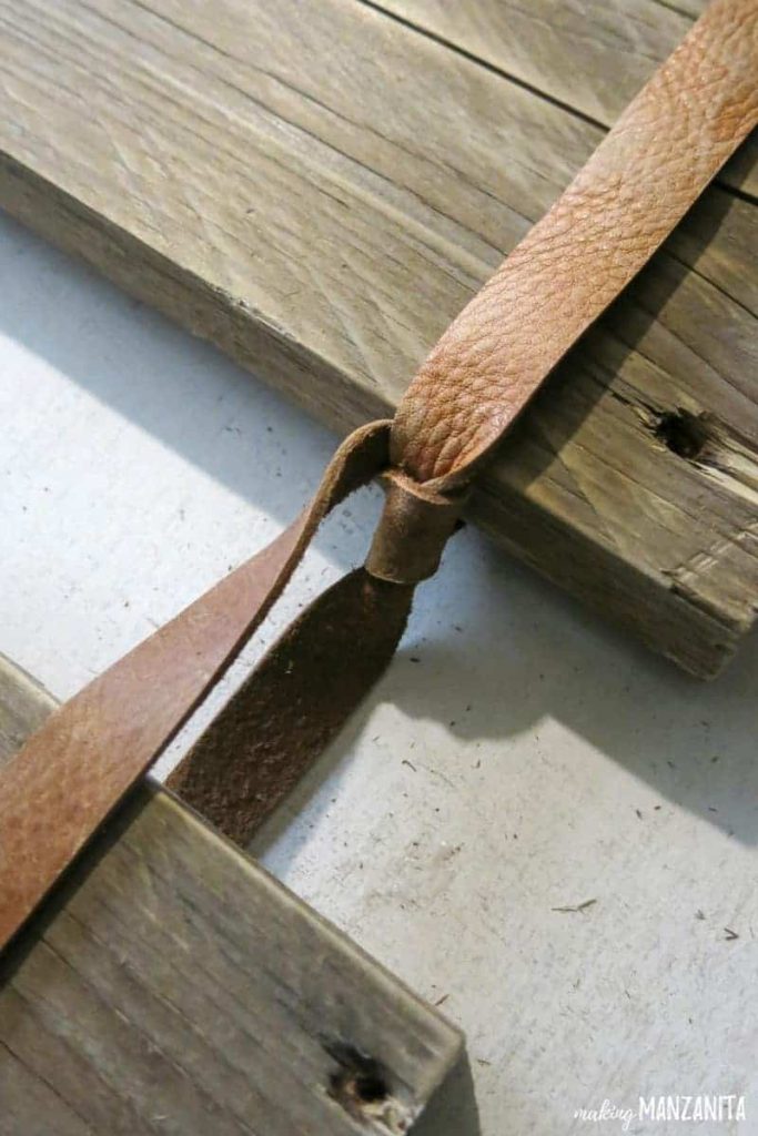 A close up image knowing a knot in a leather strip, tied around a plank of wood.