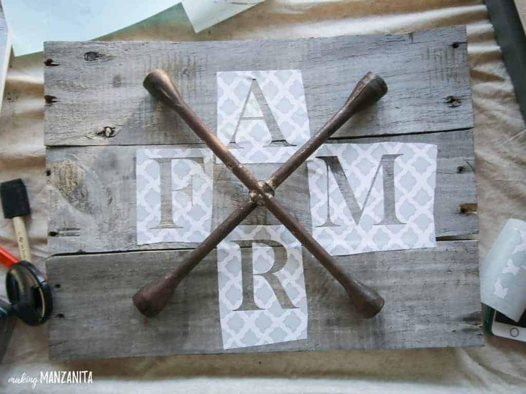 Creating the wood farmhouse style FARM sign - a lug wrench placed in the center of the pallet wood board, with stencils of letters F, A, R, and M placed around the lug wrench.