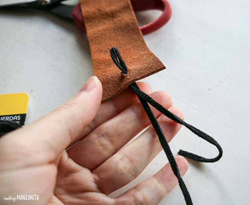 Adding a black cord string to the top of a diy leather bookmark