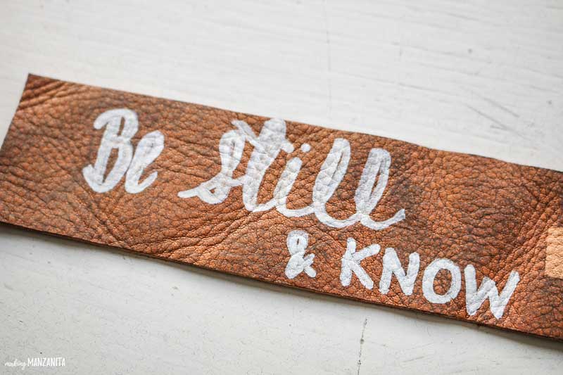 This dark-stained leather bookmark has the words be still and know written with white paint marker