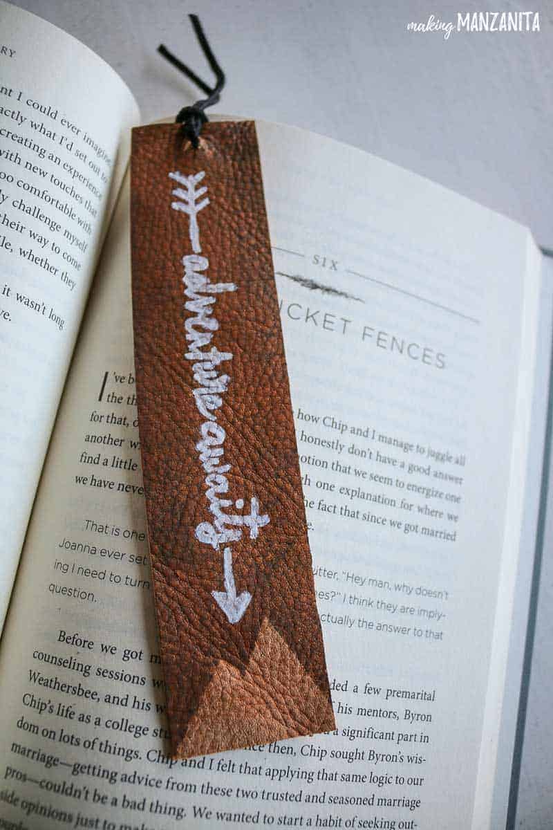 Leather bookmark with the words 'adventure awaits' written in white marker, and mountain decorations