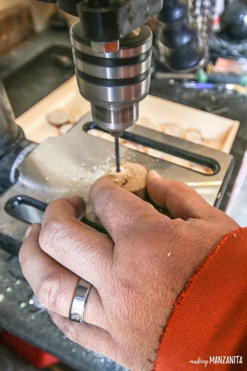 Man using drill press to drill holes in small wood rounds for the rustic advent calendar tags