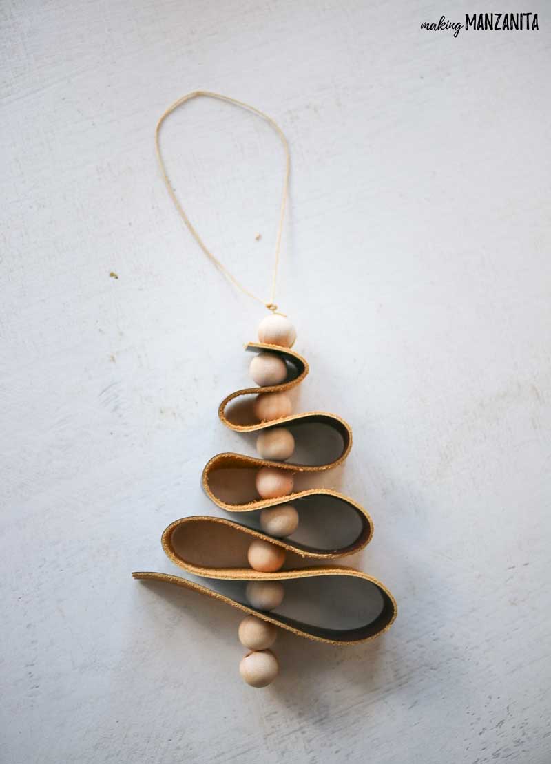 Finished leather christmas ornament made with scrap leather, wood beads and waxed string laying flat on white tabletop