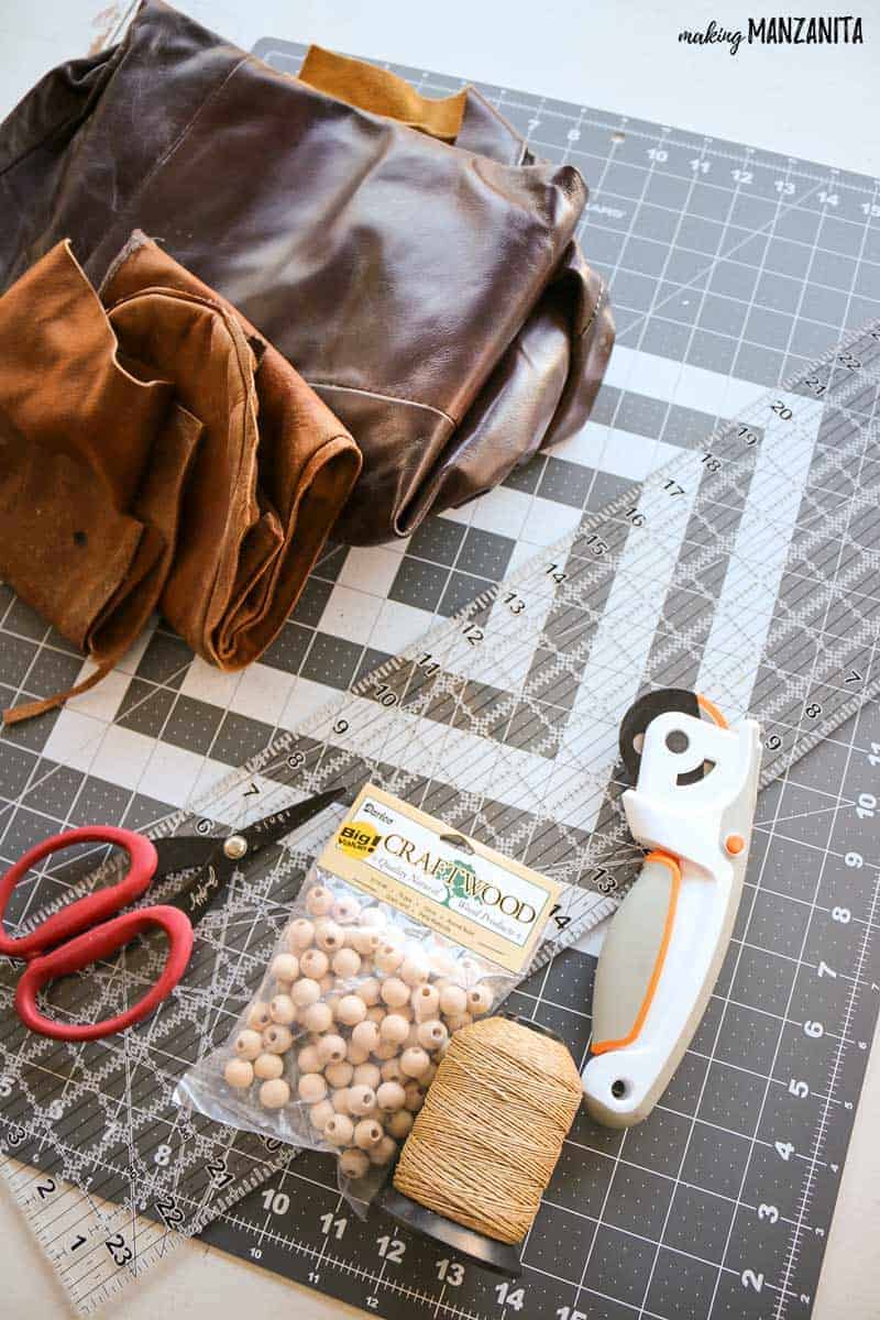 Craft supplies like rotary cutter, acrylic ruler, cutting mat, scissors, wood beads and leather flat lay on table 