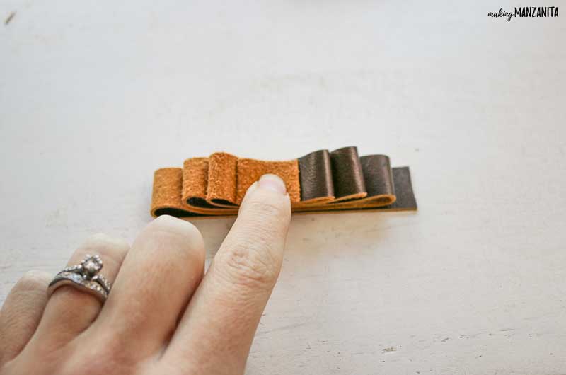 Hand holding down strip of brown leather folded up like a mini christmas tree while making a leather ornament