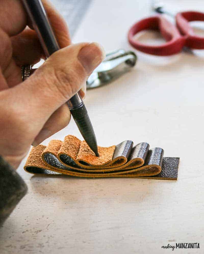 Making a mark in the leather strip folded up on table to make a leather ornament for christmas tree