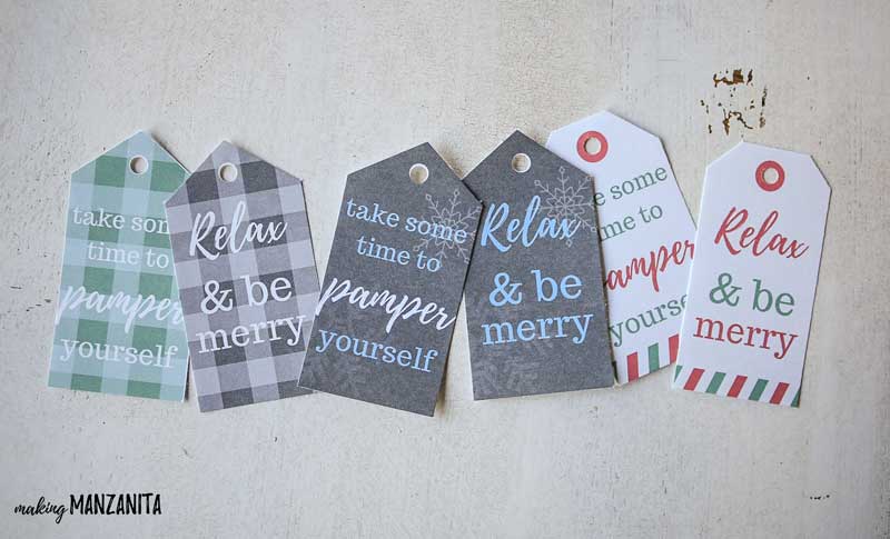 Different printable gift basket tags laying on table that say take some time to pamper yourself, relax and be merry