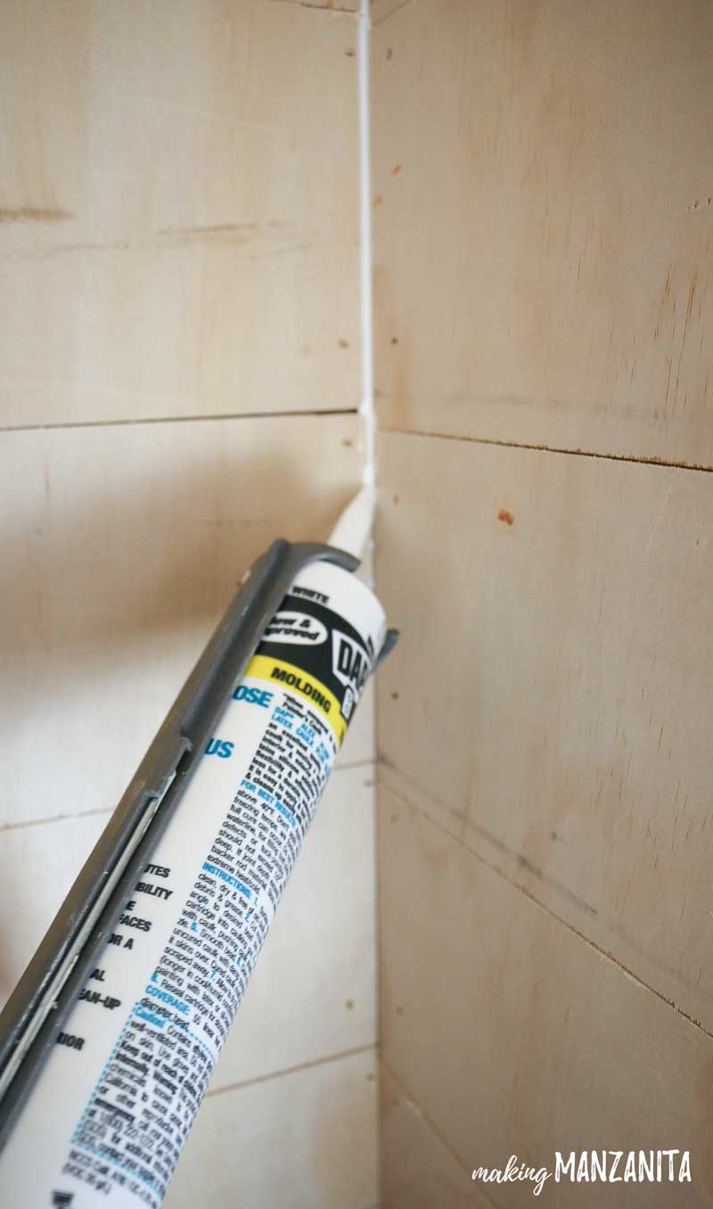 Applying caulk along the corners of the shiplap wall in the living room alcove reading nook.