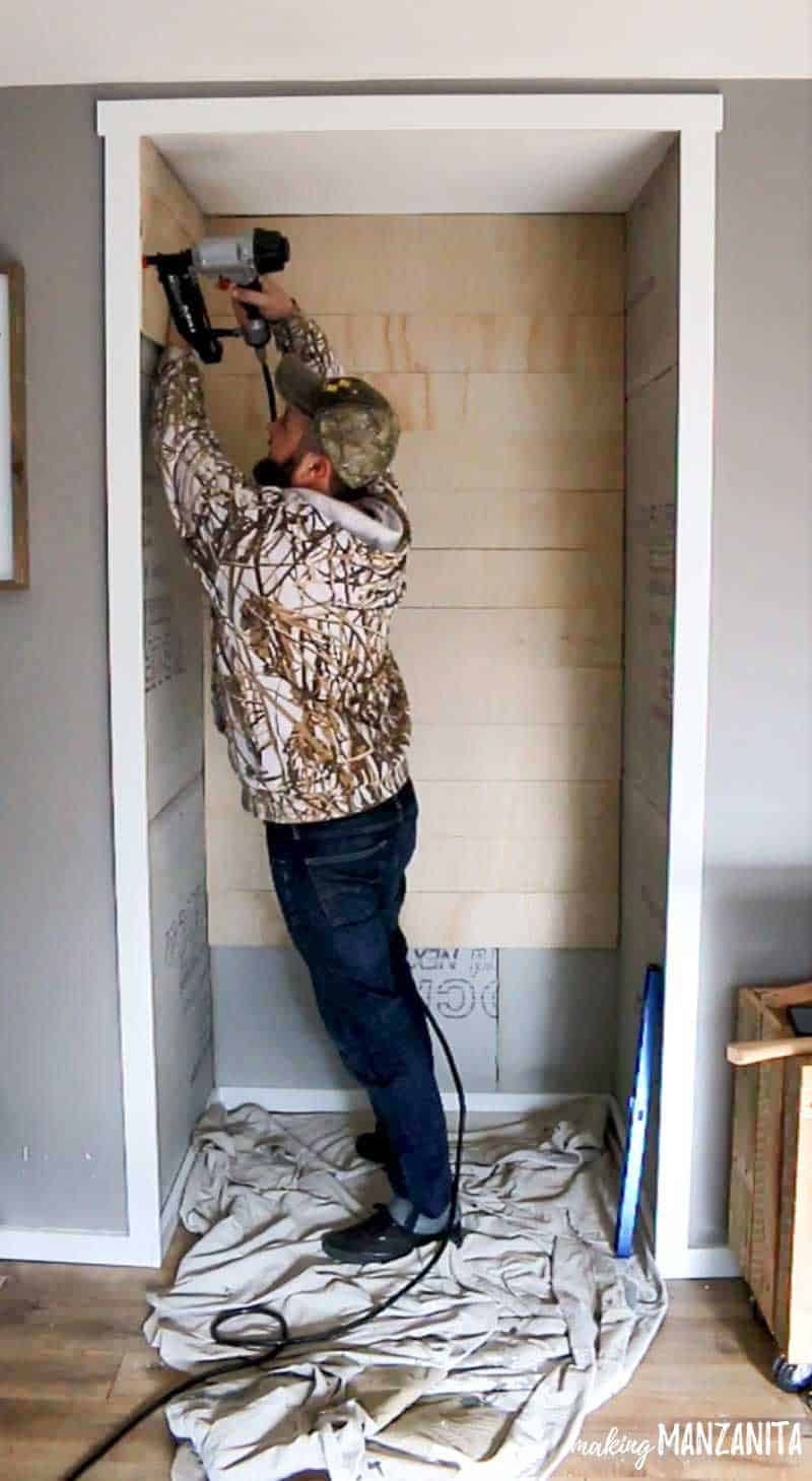 Logan begins installing the shiplap wall planks on the reading nook walls using a nail gun.