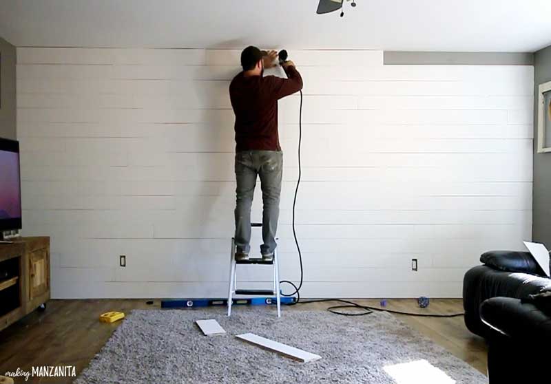 a man on a small step ladder putting up the top row of shiplap on a wall