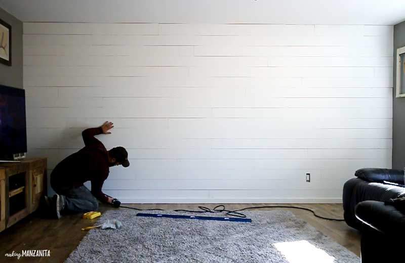 a man reinstalling the baseboard of a wall after all the shiplap has been attached