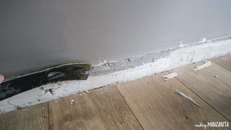 close up of a crowbar scraping down where a baseboard used to be