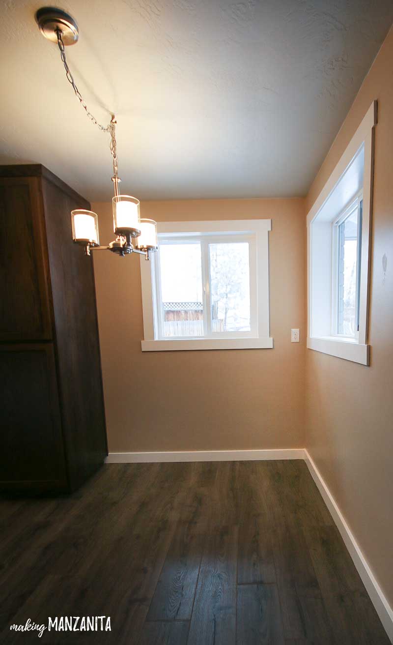 Corner breakfast nook area in kitchen with tan walls and white trim with windows and hanging light