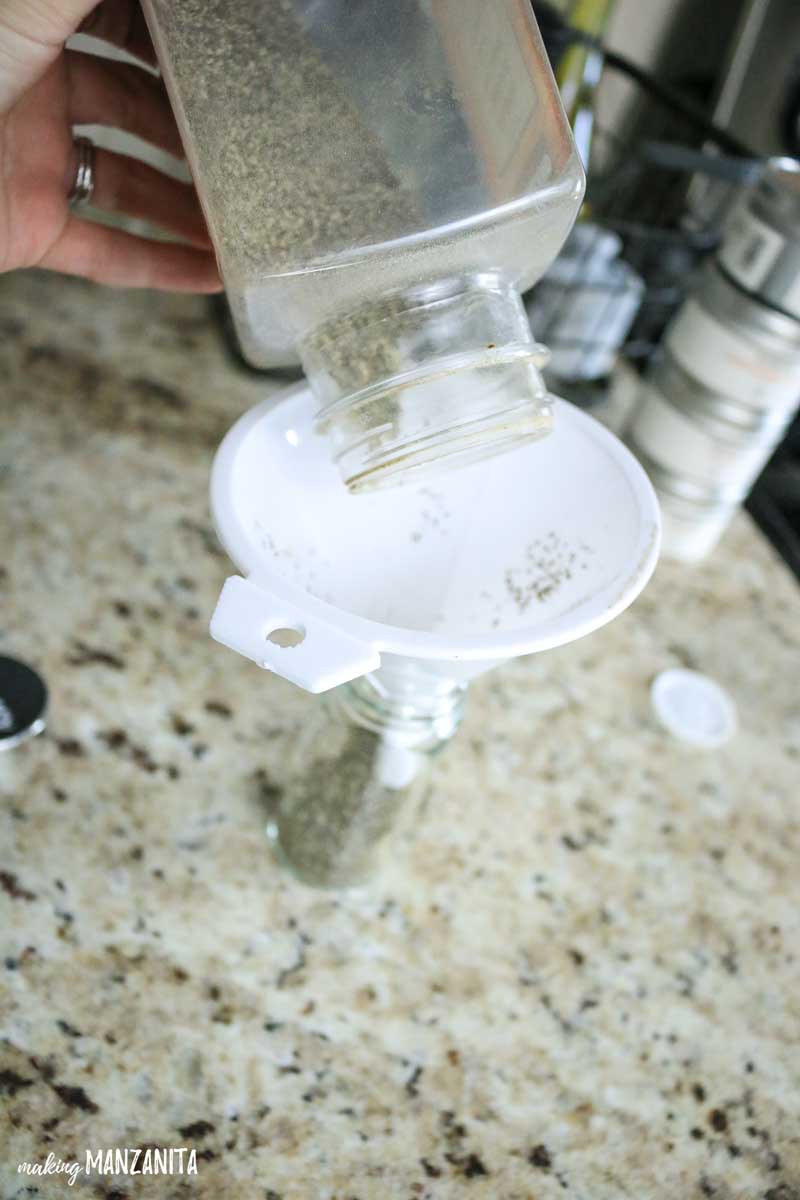 Using a small funnel to pour ground black pepper into a new spice jar.