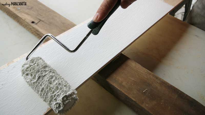 photo of a paint roller applying white paint to a 2 by 4 board