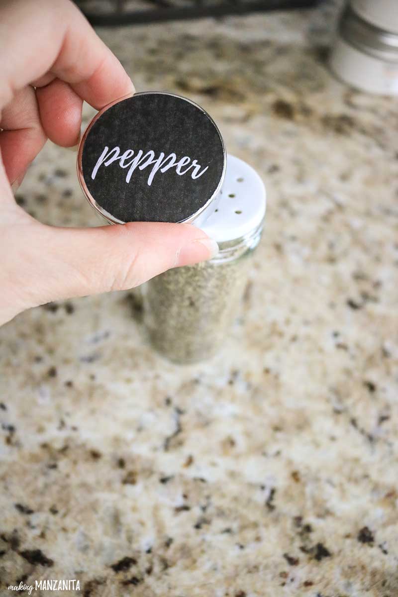 Placing a spice jar lid - clearly labeled with a spice jar label sticker that says "pepper" - on to a full spice jar.